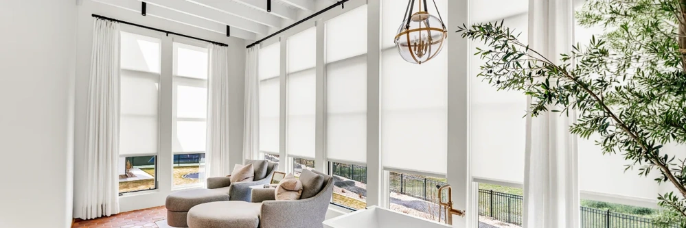 Motorized white window shades covering a wall of floor-to-ceiling windows