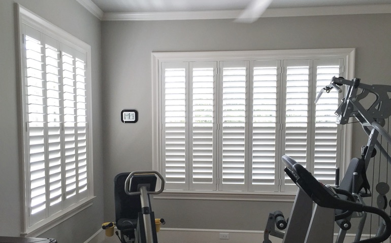 Weatherstripping window coverings are especially important in spaces with windows on more than one wall. Cleveland home gym with shuttered windows.