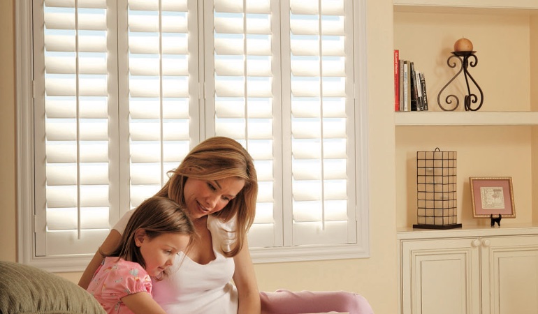 Easy to clean faux wood shutters are perfect cord-free options for children. Mom and daughter in front of window