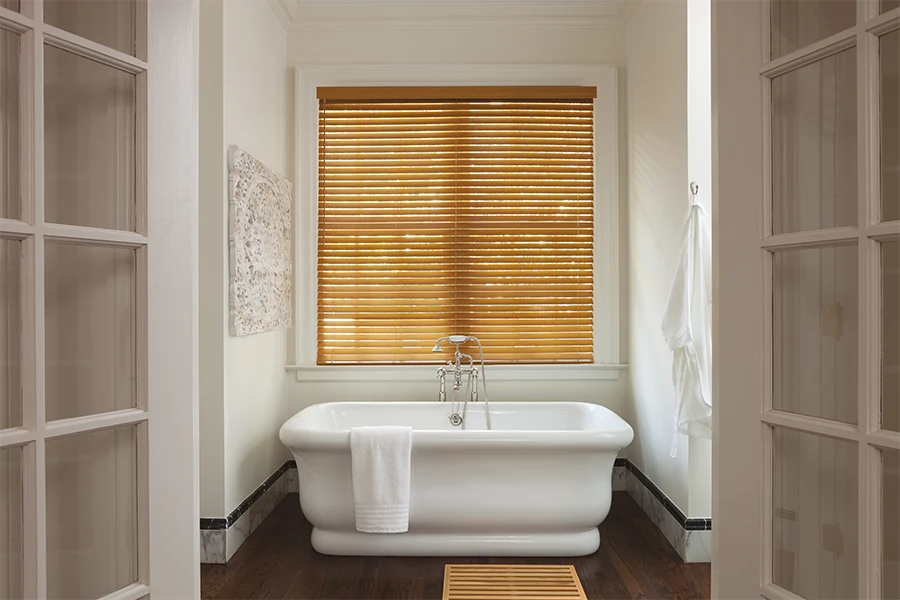 For humid rooms, always choose moisture-resistant window blinds. Brown faux-wood blinds on a bathroom window