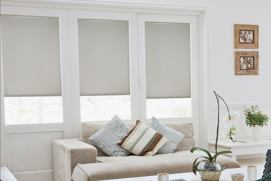Cellular shades are energy-saving for your living spaces. Light gray cellular shades on three separate windows in large light wood and beige colored living room.